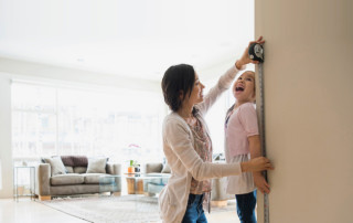 Mother measures child's height and marks door frame.